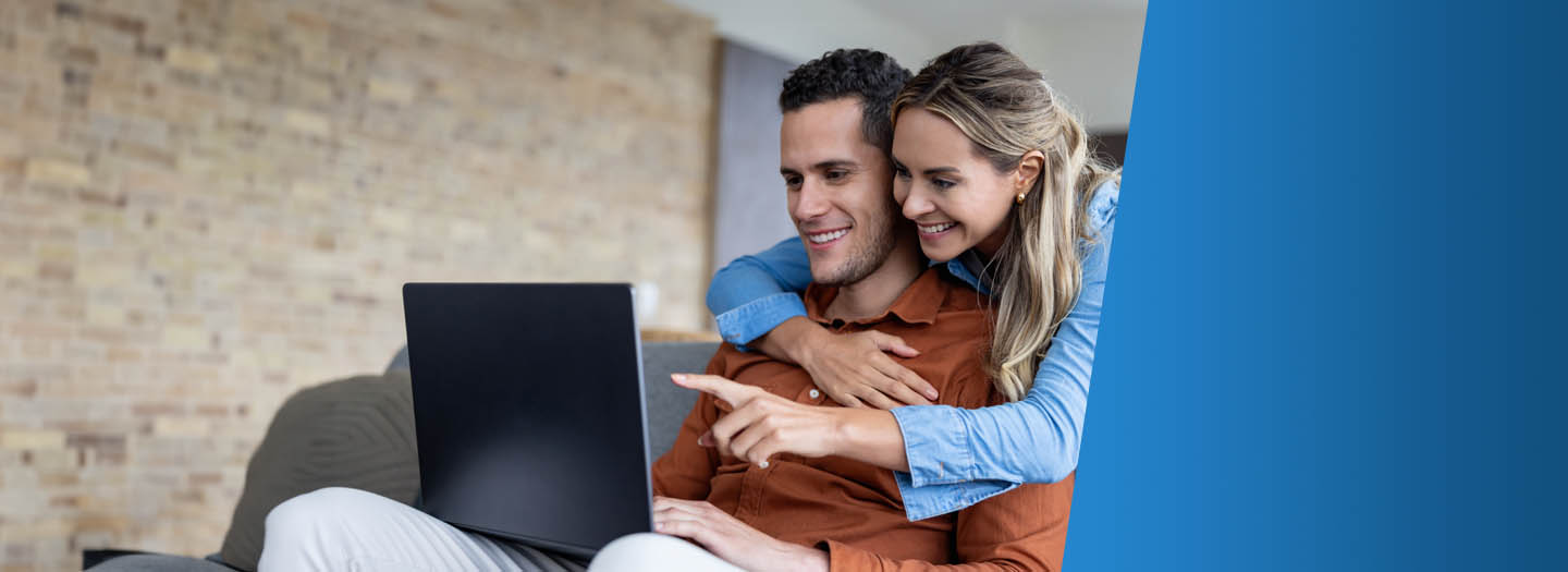 A man and a woman smiling while looking at a laptop screen